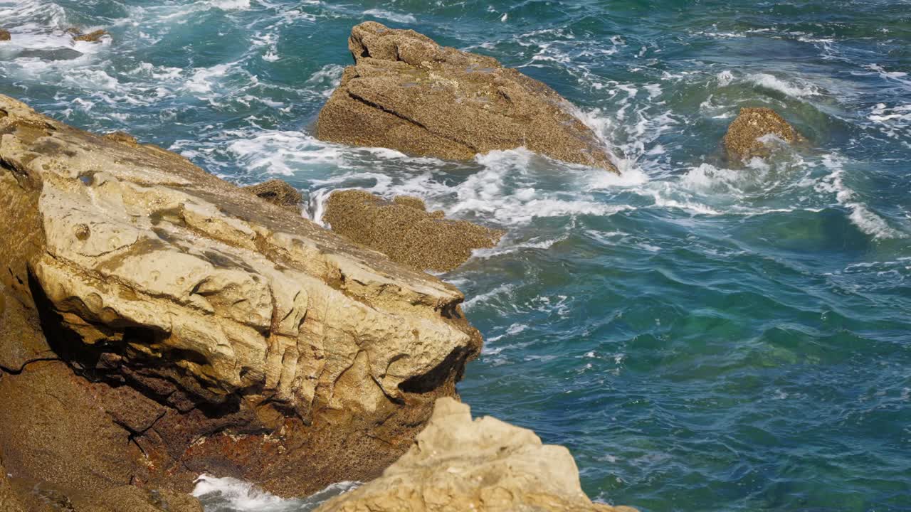 Close-up view of dark, textured rocks being hit by clear turquoise ocean waves