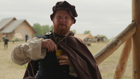 squire with red beard drinks orange elixir from glass bottle