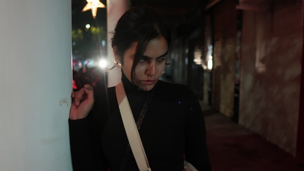 스타일리시한 젊은 여성이 음모의 공기와 함께 희미하게 밝은 골목길에서 모이를 둘러보고 있습니다.