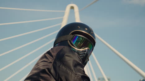 person in a motorcycle helmet with iridescent goggles looking at a modern bridge