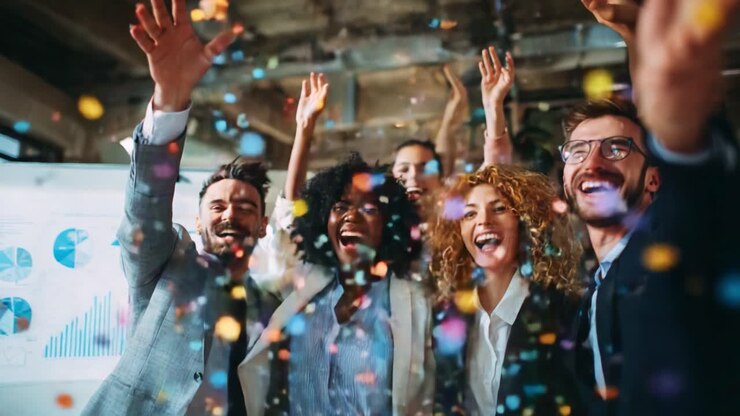 Celebration of Success: A Joyful Group of Professionals Exchanging Enthusiasm and Happiness Amidst Colorful Confetti in a Dynamic Office Environment
