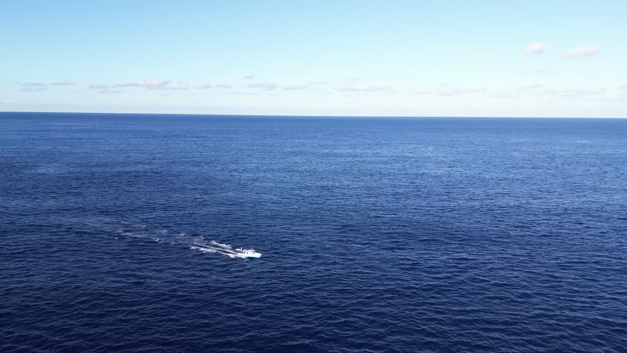 A boat travels across the calm blue ocean under a clear sky.