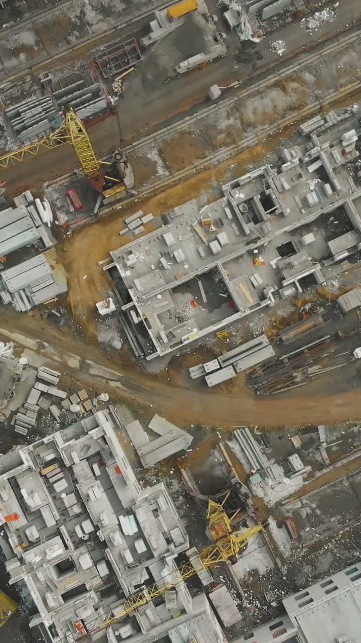 gray block building site with equipment and big yellow construction cranes on cloudy spring day bird eye view