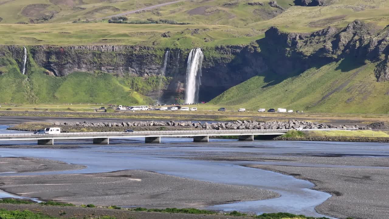 Cars on Bridge crossing River with Seljalandsfoss waterfall, Iceland. Aerial wide shot. Sunny day in autumn season