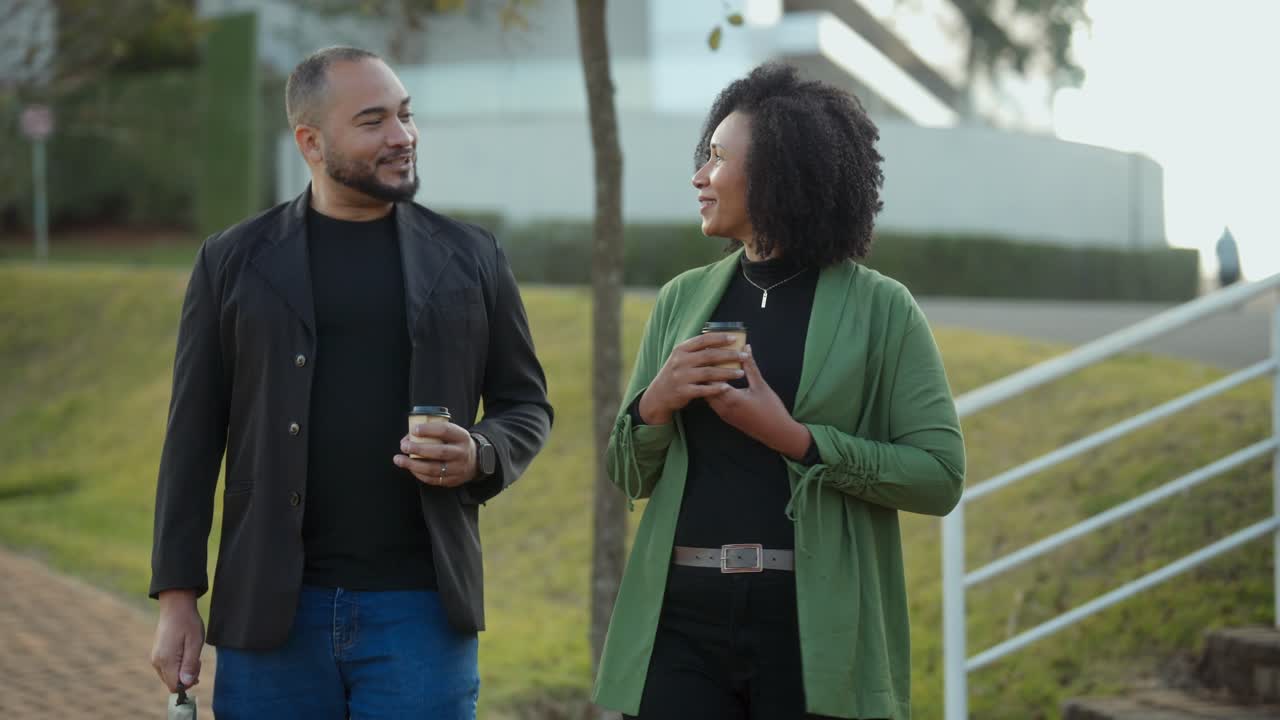 Two people walking and having a conversation while drinking coffee