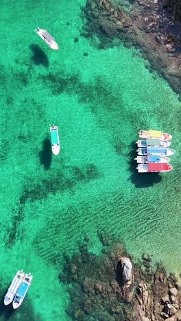 Boats-over-a-beach-with-a-coral-reef-from-the-air,-vertical-mode