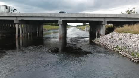 aerial starting underneath a bridge on a canal pulling back to reveal cars going over bridge with canal and its surrounding area