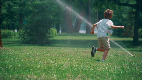 active little boy running playing with dog on field with sprinklers on sunny day