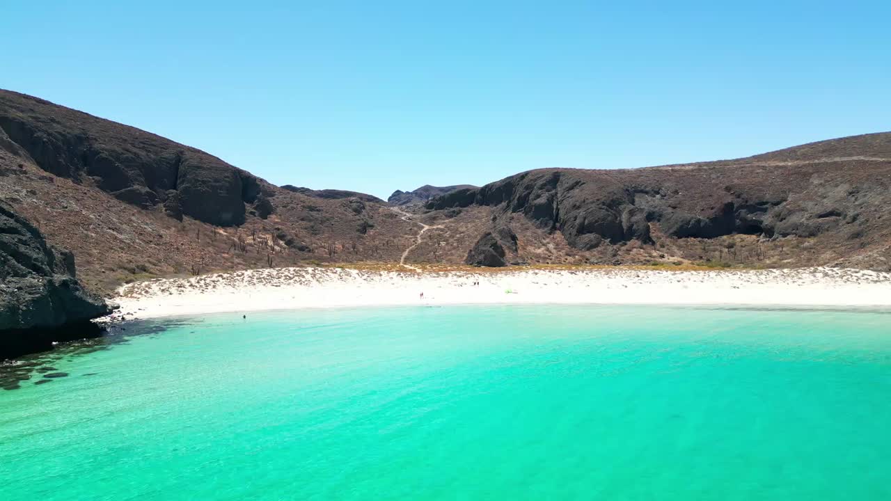 Crystal-clear turquoise water meets a sandy beach framed by rugged mountains in Tecolotito, La Paz