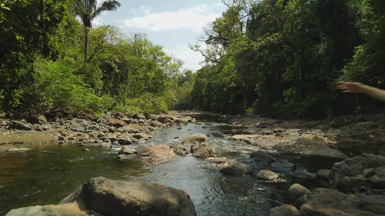 drone vuela a través del exuberante río de la jungla con una modelo femenina atlética posando con los brazos en alto, 4k costa rica