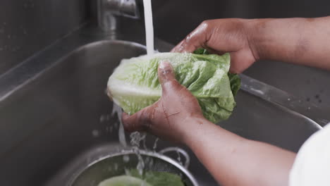 African-american-male-chef-washing-vegetables-in-sink-in-kitchen,-slow-motion