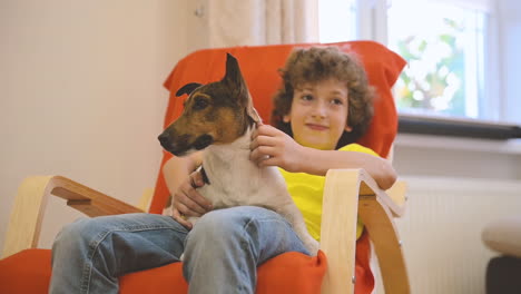 blond boy sitting on the chair while swinging with his dog and caresses him 1