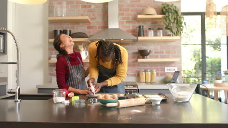 Happy-diverse-couple-in-aprons-decorating-christmas-cookies-in-kitchen,-copy-space,-slow-motion