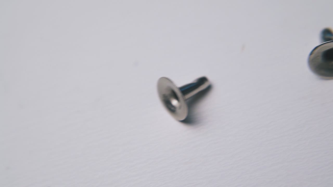 рассеянные блестящие металлические заклепки лежат на чистой светлой поверхности