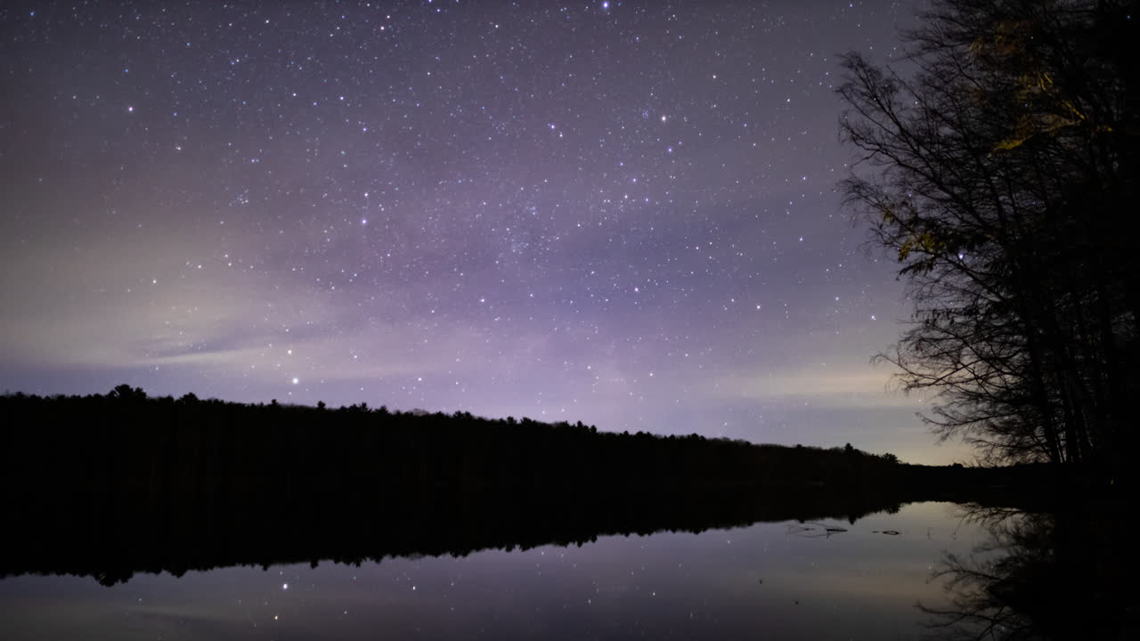 um lapso de tempo de uma fina camada de nuvens se movendo sobre um pequeno lago, obscurecendo as estrelas enquanto elas se movem pelo céu