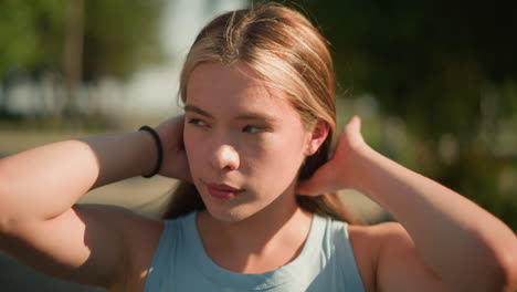 close-up of lady parking her hair to the back while glancing into distance, with sunlight reflecting on her hands, wearing a black hand bangle, softly blurred background featuring greenery