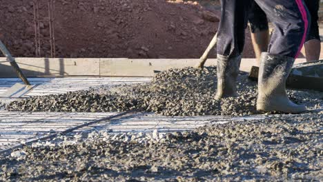 Construction-workers-pulling-mixed-cement-and-gravel,-spreading-it-over-a-floor-layout-of-a-building-under-construction-in-Southeast-Asia