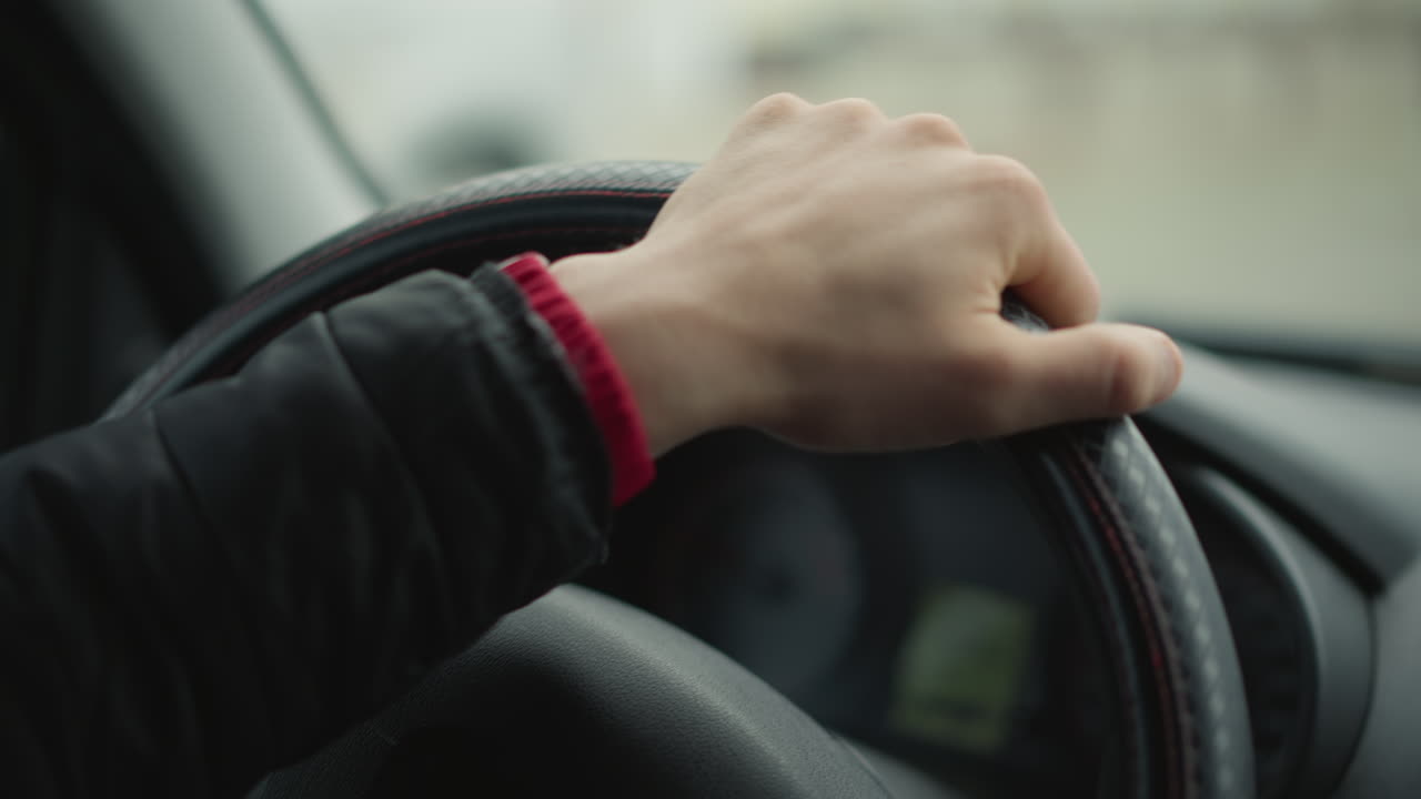 Male driver hands firmly gripping steering wheel as he turns it sideways with precise smooth motion, background blurred traffic and cars creating dynamic driving atmosphere and emphasizing control