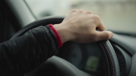 male driver hands firmly gripping steering wheel as he turns it sideways with precise smooth motion, background blurred traffic and cars creating dynamic driving atmosphere and emphasizing control