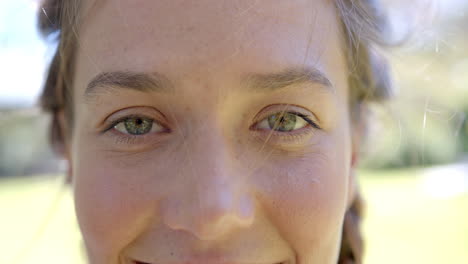 close-up of woman face with green eyes, smiling outdoors in sunlight