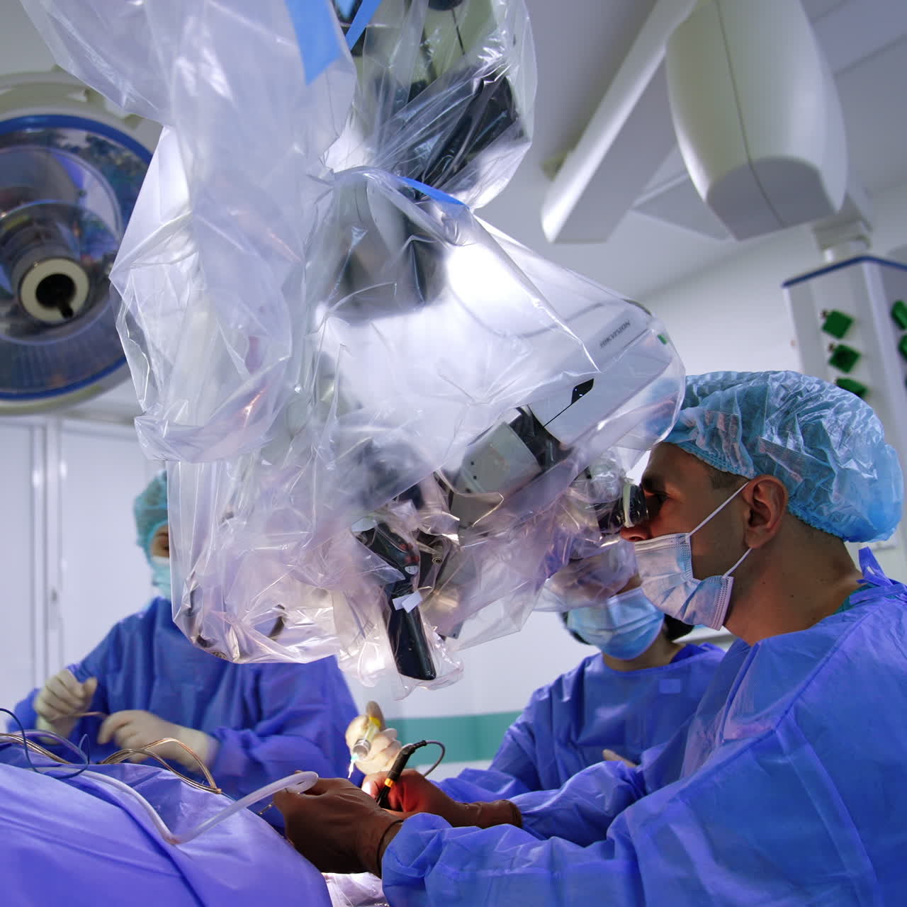 Professionel kirurg udfører neurokirurgisk operation på hjernen. Lægen kigger opmærksomt i mikroskopet og anvender værktøjer.