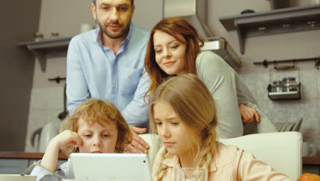 niño y niña sentados en la cocina usando una laptop mostrando algo a sus padres