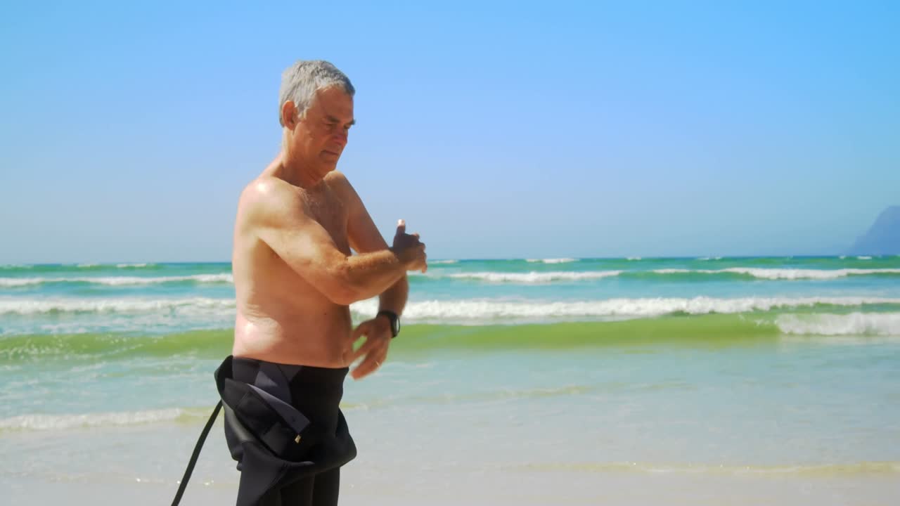 해변 에 서 있는 활동적 인 고위 백인 남성 서퍼 의 측면 뷰 4k