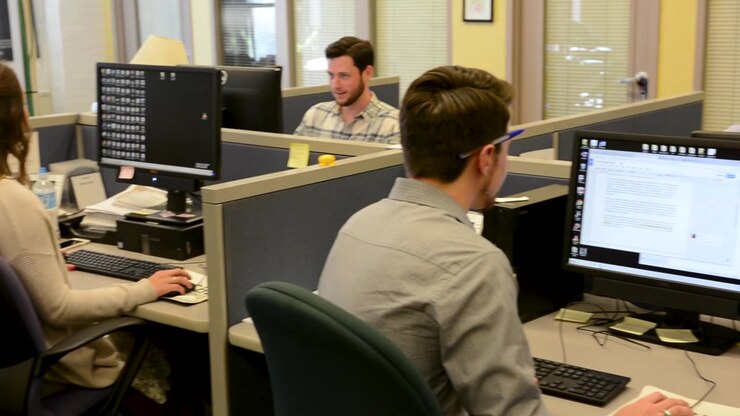 Left panning shot of young professionals working in cubicles on computers