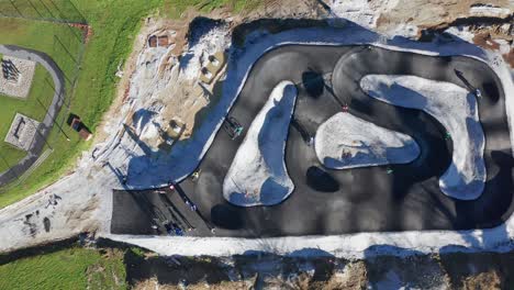 children, unrecognizable, ride bicycles on pump track still under construction, urban recreation and outdoor fun, offroad bike skills and recreation, aerial zoom out