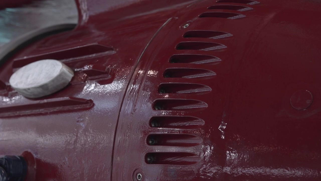 Tight angled view of heavy industrial machinery with reflective painted metal surfaces, visible fasteners, mounting hardware, and soft neutral light inside technical workshop setting