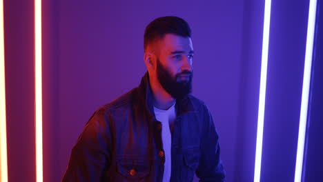 close up view of young man standing among neon lights and smiling cheerfully to the camera