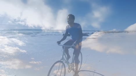 Animation-of-clouds-over-happy-african-american-man-with-bike-on-beach