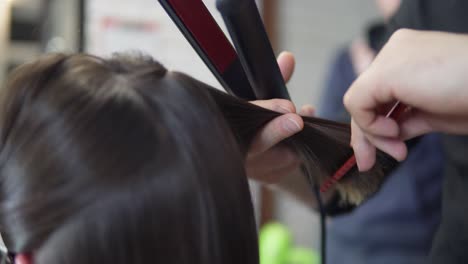 Professional-hairdresser,-stylist-makes-professional-hairstyle-of-young-woman-in-beauty-studio,-using-barrette-for-fixing-hairdo.-Hair-straightening-Beauty-and-haircare-concept