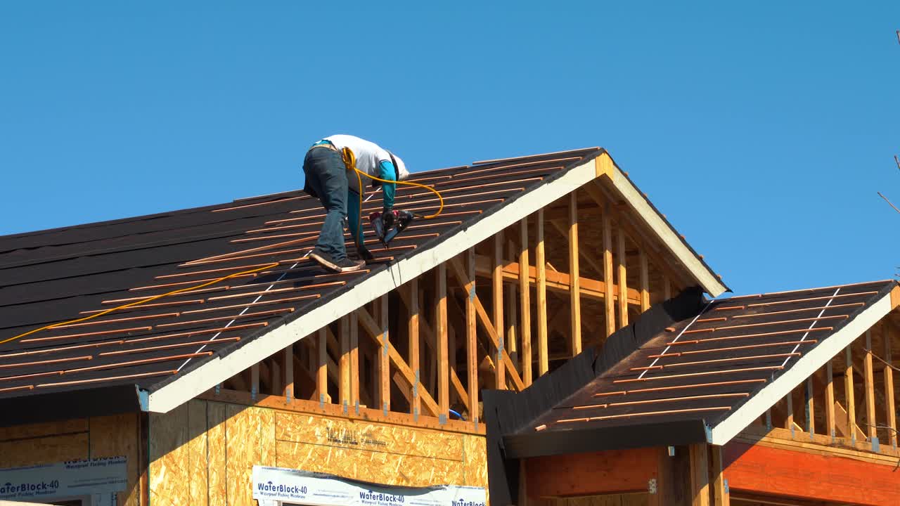 Worker nailing wood slats for installation of ceramic roofing tiles on residential building using an air nail gun- new home roof construction in California shot in 4K