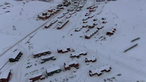 Vista-De-Drones-En-Svalbard-Volando-Sobre-La-Ciudad-De-Longyearbyen-Mostrando-Casas-En-Una-Zona-Nevada-Con-Un-Fiordo-Y-Una-Montaña-En-Noruega