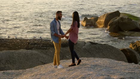 Paar-Gemischter-Abstammung-Hält-Händchen,-Während-Es-Auf-Einem-Felsen-Am-Strand-Steht-4k