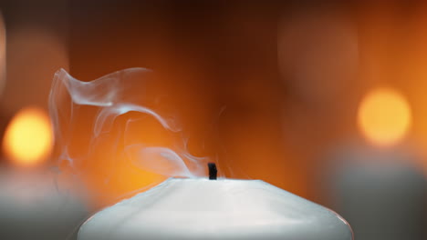 blowing out a white candle in macro and slow motion, thick smoke rises from burnt wick against warm candlelight