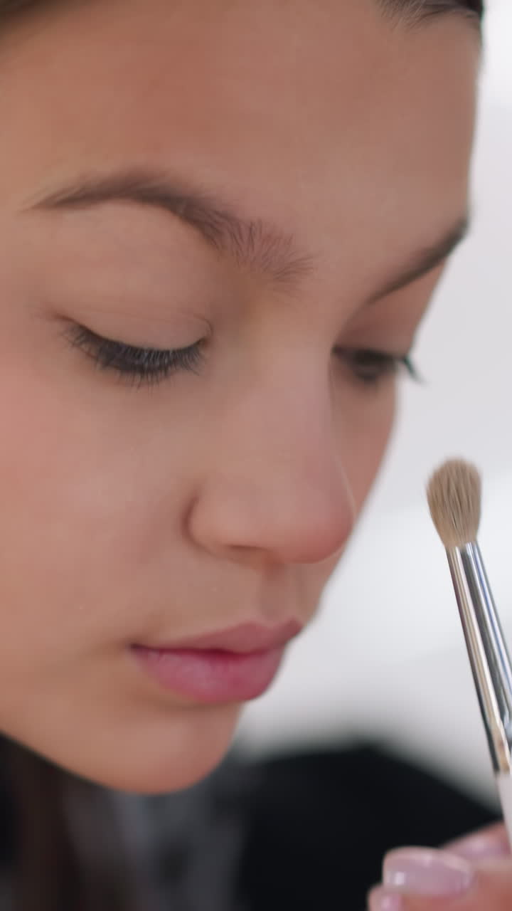 Primer plano de una joven maquillándose por la mañana con una paleta neutra suave; delicadas pinceladas sobre el párpado; ambiente tranquilo y reflexivo; acabado jugoso; difuminado cuidadoso; sutil iluminador en el arco superciliar