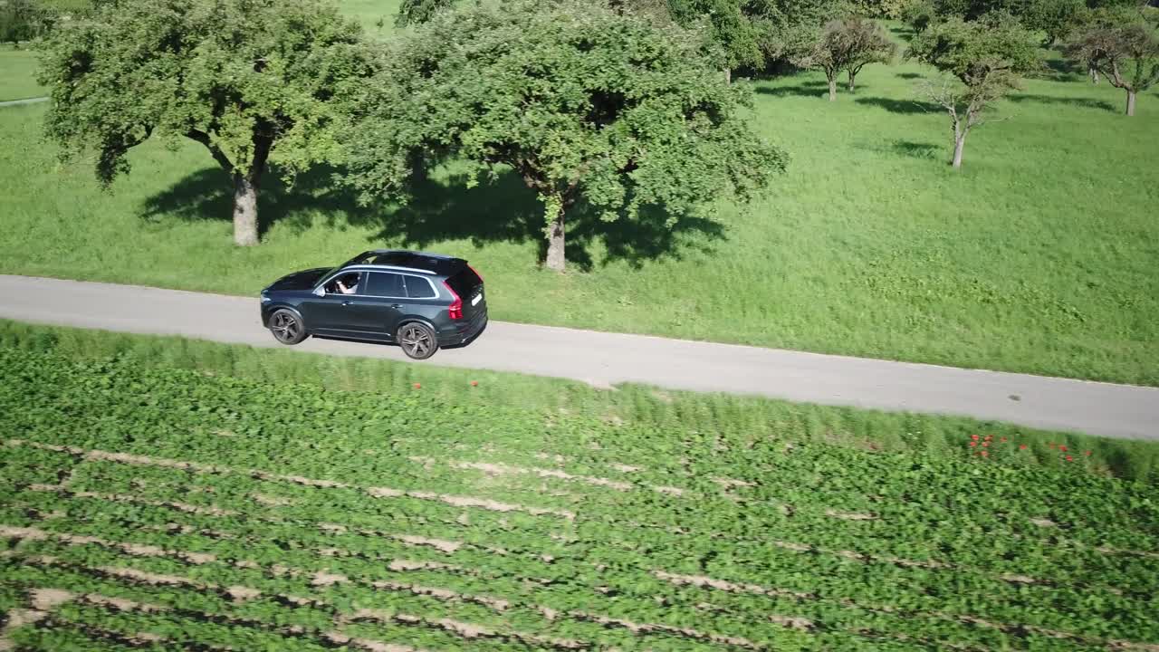 un camión volvo xc 90 conduce por una pequeña carretera llena de baches entre campos, pocos árboles, campiña suiza, vaud, vista aérea de drones