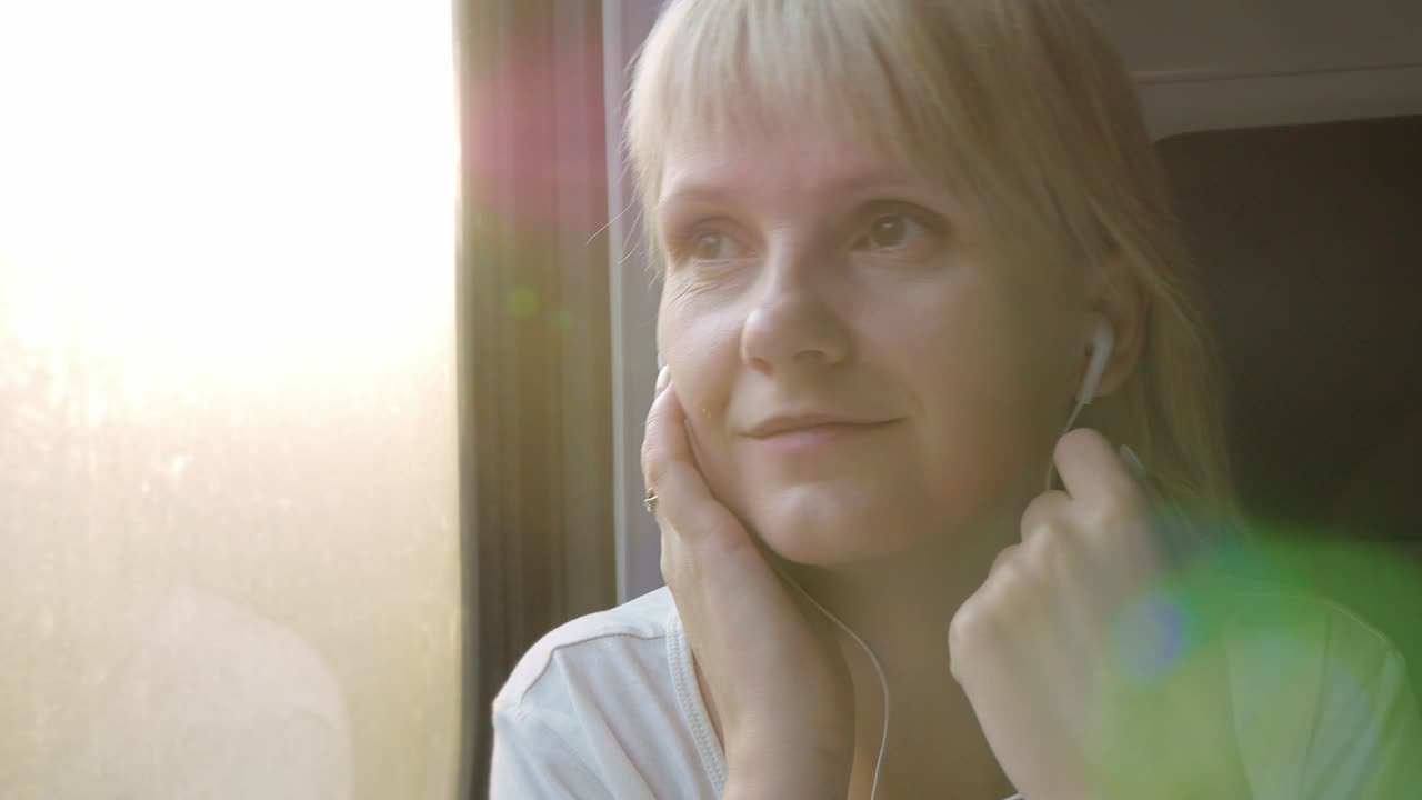 A woman listens to music on headphones, looks out the window from a traveling train. Travel and holiday concept