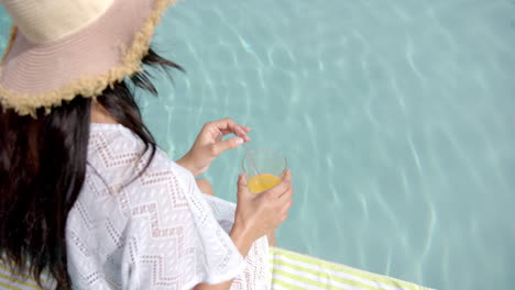 biracial teenage girl in sunhat drinking juice by pool, copy space, slow motion