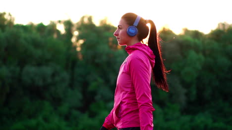 a girl in a pink jacket is preparing for a run warm up and listen to music in headphones through the phone