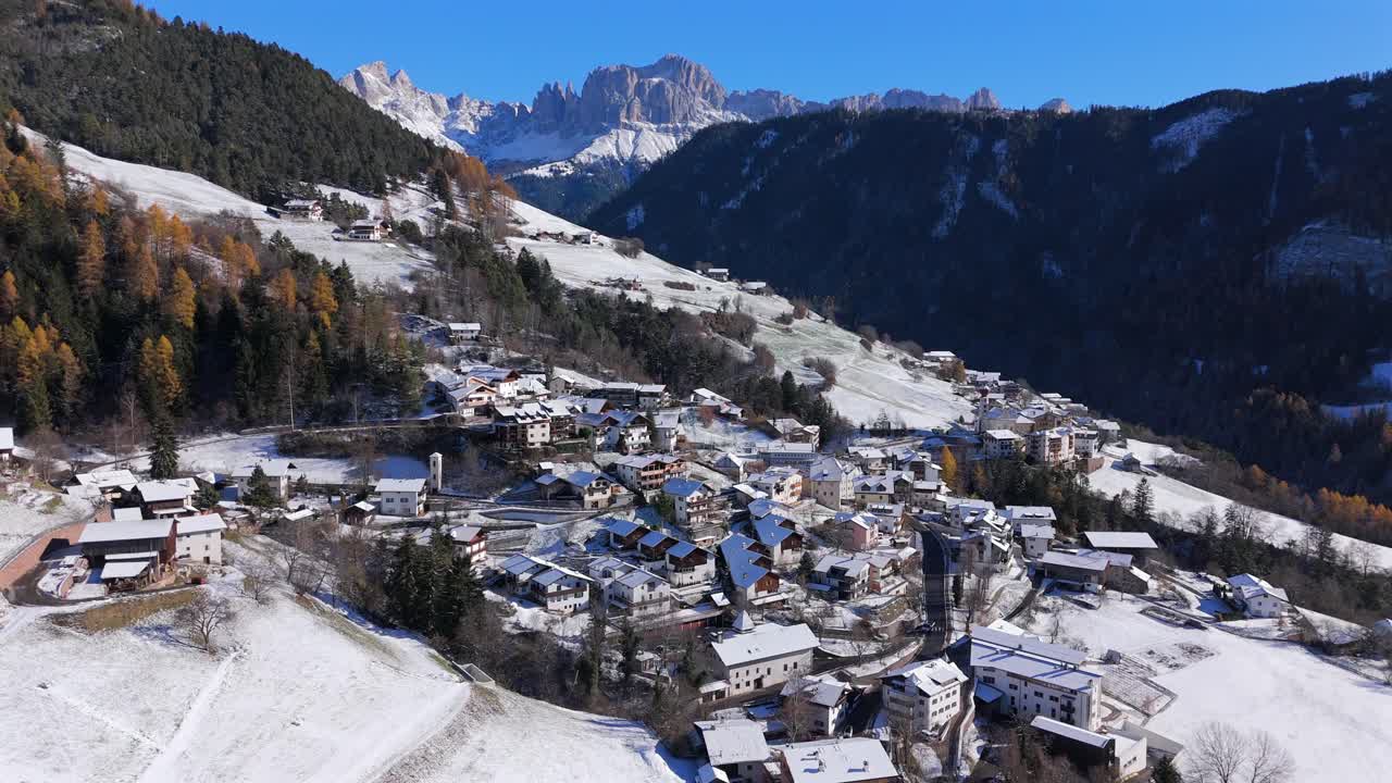 Slow motion 4K drone shot over the snow-covered alpine village of Tiers Tires in South Tyrol Alto Adige Italy with Rosengarten Catinaccio peaks and soft winter light in the Dolomites