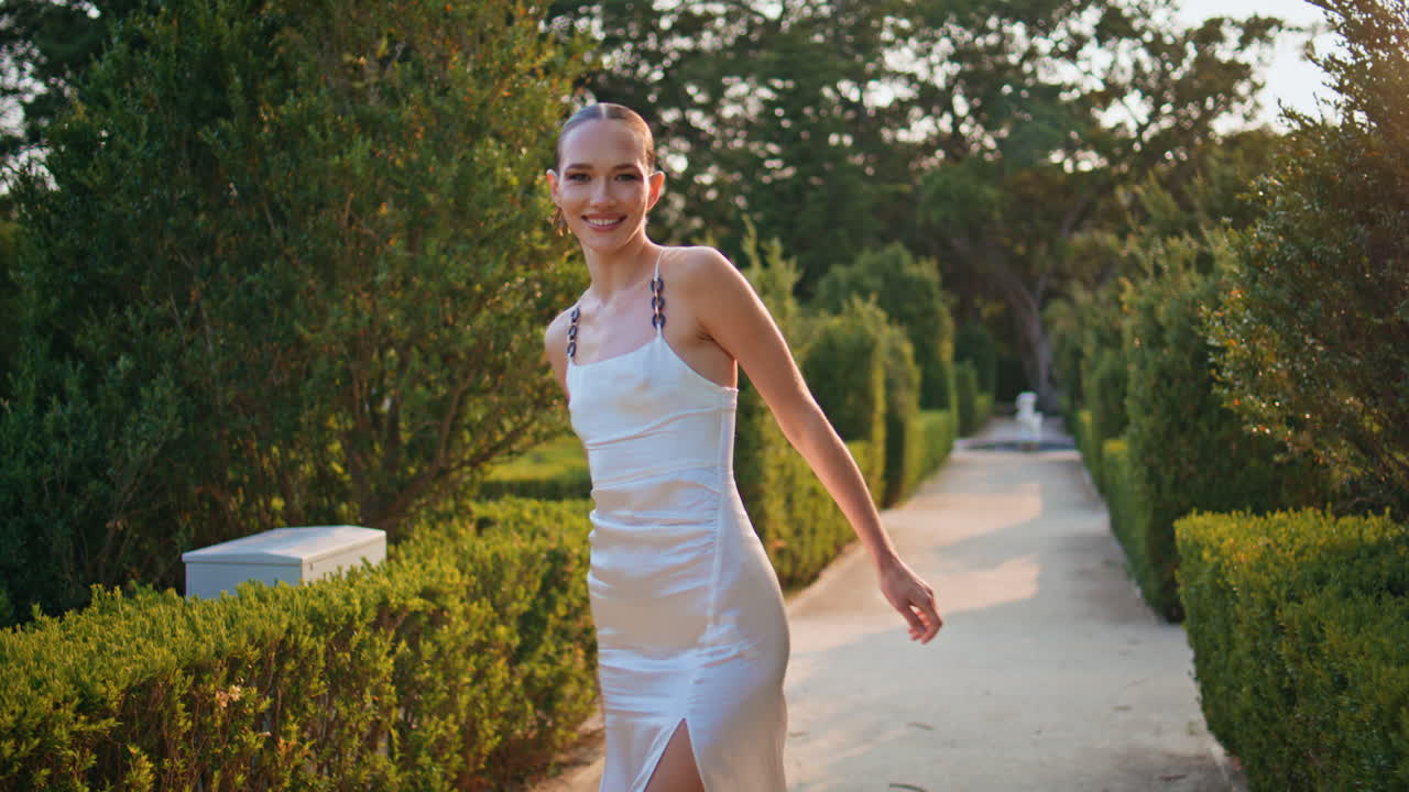 무관심한 소녀가 공원에서 돌아다니며 행복한 미소로 카메라를 쳐다보고 있다. 웃는 여자