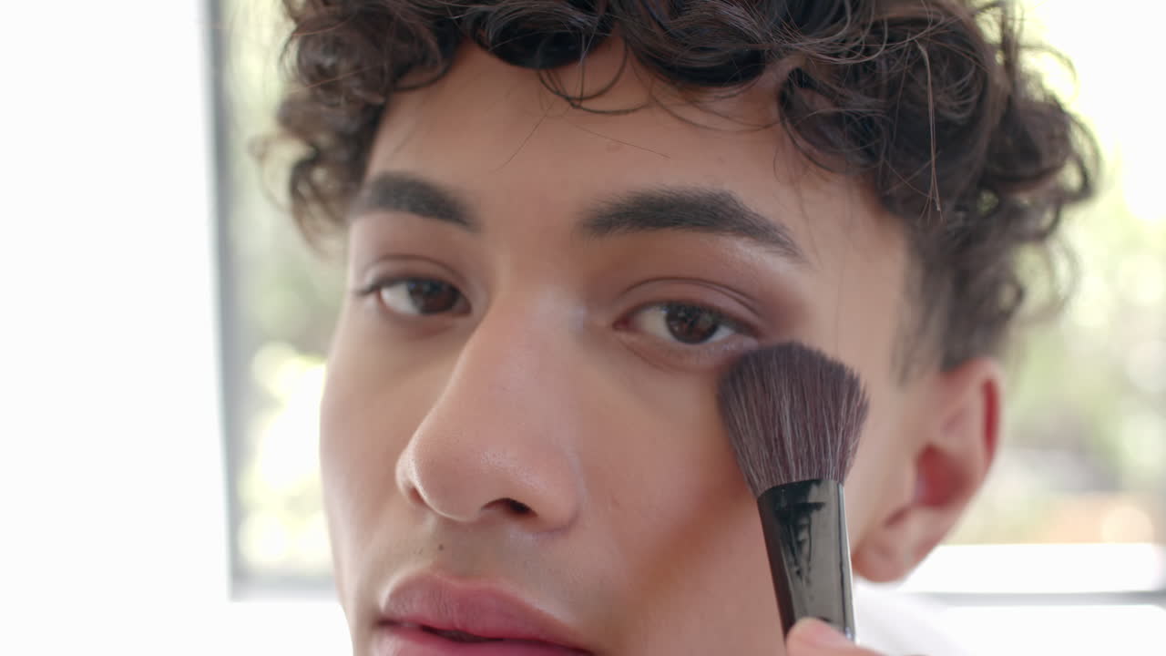 Applying makeup with brush, non binary person focusing on face in close-up shot
