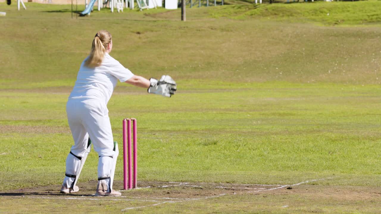 Playing cricket, female wicketkeeper in action on field, catching ball
