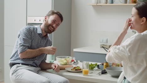 laughing couple playing and having fun together sitting on stool in a modern kitchen