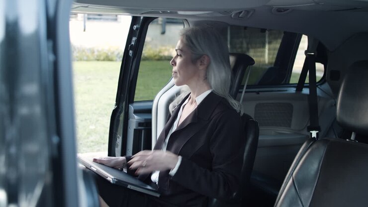 Donna dai capelli grigi con un laptop in tailleur che sale in auto