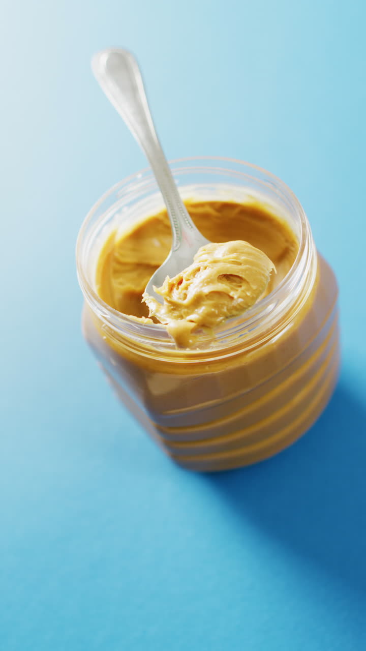 Vertical video of close up of peanut butter on blue background