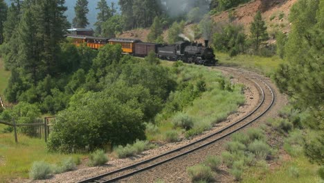 a steam train moves around a curve in the rocky mountains